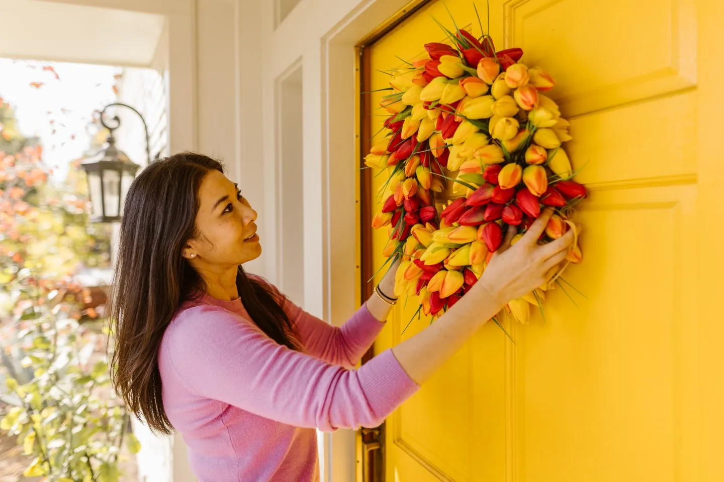 Person hanging a colourful wreath on a yellow front door