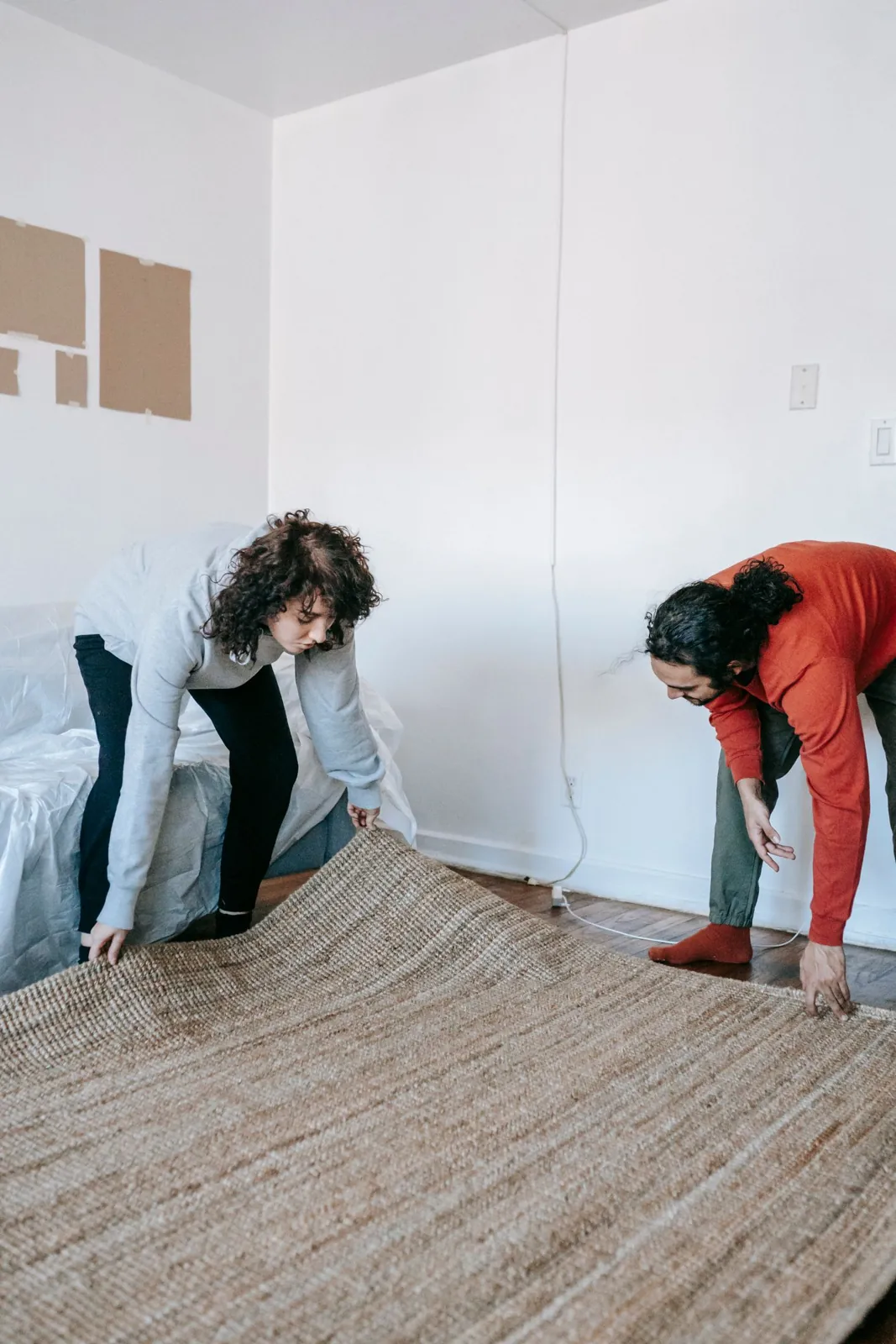 Two people positioning a woven rug on the floor