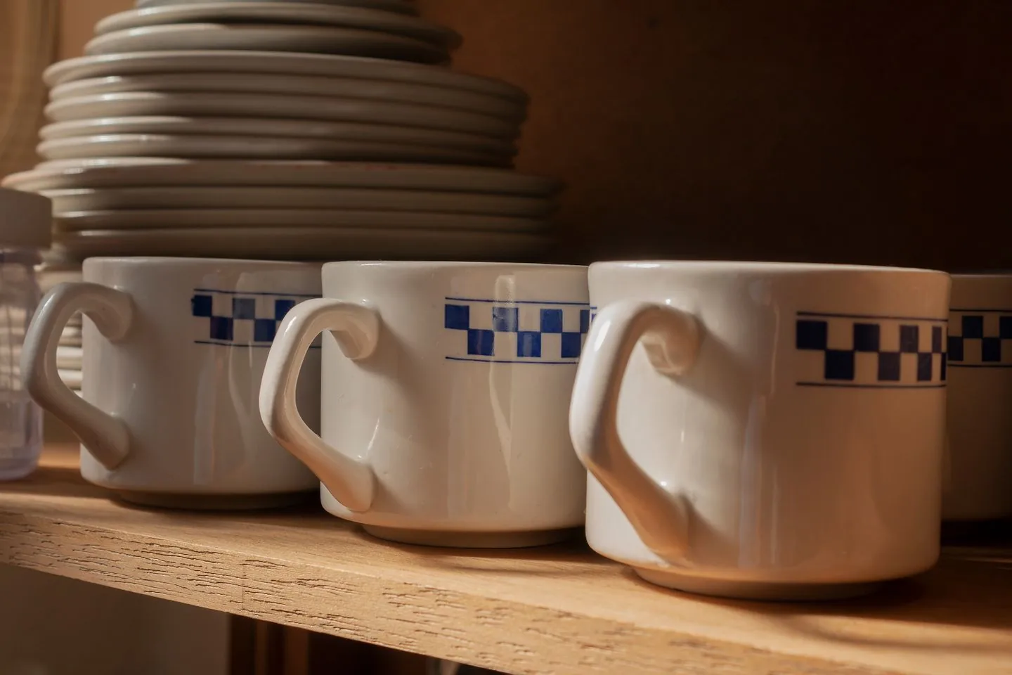 Ceramic mugs lined up below a stack of plates